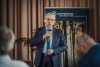 Grupa dzieci siedzi wokół dużego stołu pokrytego szarym papierem, intensywnie pracując nad rysunkami. Na środku leżą białe kartki z konturami różnych liści drzew, które uczestnicy kolorują lub przerysowują. Widok z góry ukazuje skupienie uczestników, ich dłonie z kredkami oraz rozłożone materiały edukacyjne.