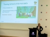 Prelegent stojący przy mównicy w sali konferencyjnej, obok dużego ekranu z prezentacją. Na slajdzie widoczny tytuł „Traning School of EU-PoTaRCh”, informacja o „2nd EU‑PoTaRCh TS”, temat „Environmental History of Resins and Charcoal” oraz lokalizacja „Gutenstein, Austria”. W centralnej części slajdu umieszczone jest zdjęcie grupowe wykonane w lesie. Mównica ma ekran z logo „Universitatea Transilvania din Brașov”. W tle jasna ściana z niewielkimi kolorowymi kwadratami stanowiącymi element dekoracyjny.