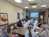 Prelegent stojący na końcu sali konferencyjnej omawia slajd wyświetlany na ekranie projekcyjnym, zatytułowany „Technical Service”. Liczna grupa studentów siedzi po obu stronach długiego, drewnianego stołu, robiąc notatki i słuchając wykładu. Na blacie, pomiędzy materiałami szkoleniowymi i butelkami z wodą mineralną, ustawiono rzędy białych toreb upominkowych. Wnętrze sali uzupełniają wiszące na ścianach plakaty informacyjne firmy Sherwin-Williams oraz duży, nowoczesny obraz w ciemnej ramie.