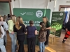 Grupa uczennic odwiedza stoisko Wydziału Leśnego i Technologii Drewna Uniwersytetu Przyrodniczego w Poznaniu. Przedstawicielka uczelni pochyla się nad blatem, tłumacząc szczegóły oferty edukacyjnej zgromadzonym dziewczętom. Całość odbywa się na tle zielonej ścianki reklamowej oraz roll-upu z wyraźnymi logotypami wydziału.